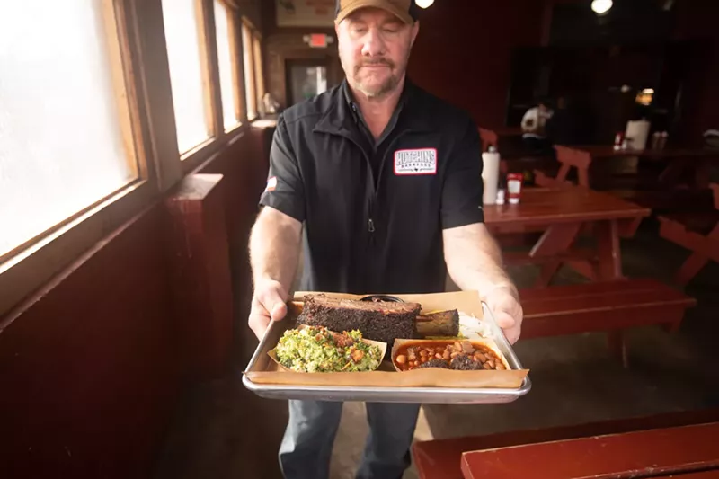 Image: Trey Hutchins holds a sampling of the fare that keeps Hutchins BBQ on our list of Top 100 Restaurants.