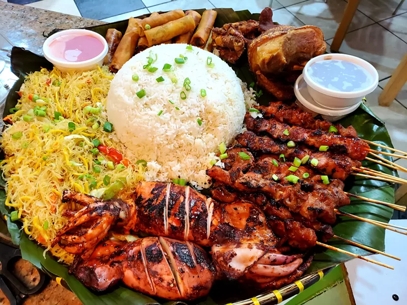 Image: Kanin’s Boodle Bila-o: pancit, lumpia, crispy pata, pork BBQ sticks, inihaw na pusit (grilled squid) and various sasawans encircling a bed of rice