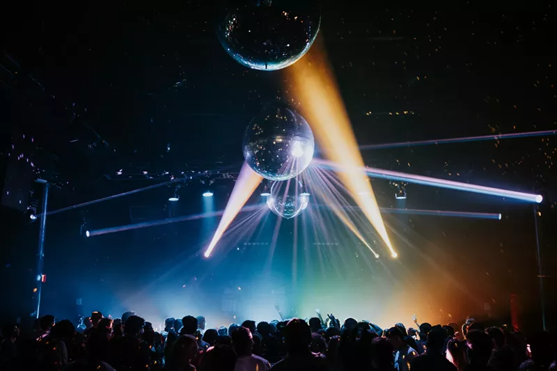 Image: A crowd dances at a rave under disco balls.