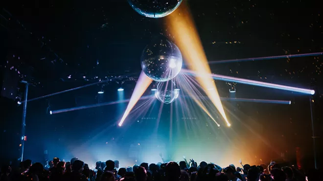 A crowd dances at a rave under disco balls.