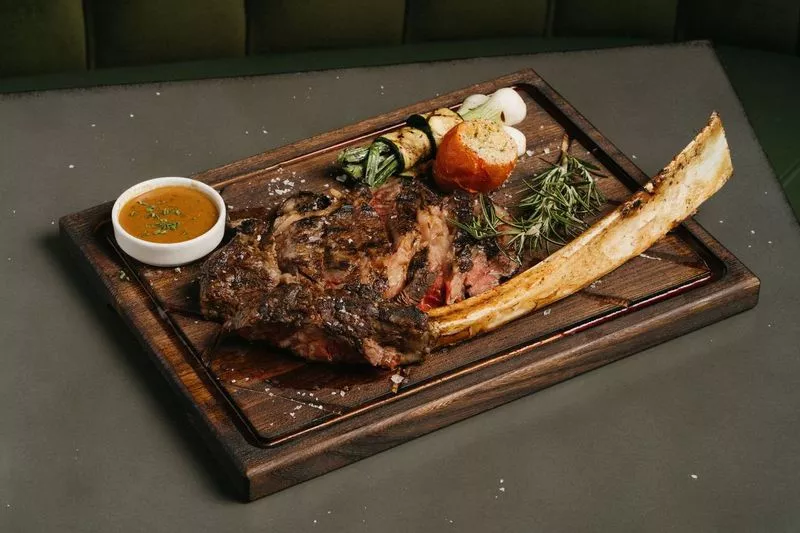 Image: The GOAT's 32-ounce Tomahawk ribeye can be gussied up with optional add-ons of Sauce au Poivre, made with cognac, pepper and cream, or buttery Sauce L'Entrecôte, which the menu says has flavors of umami and herbs.