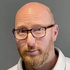 A headshot of a man with glasses and a beard