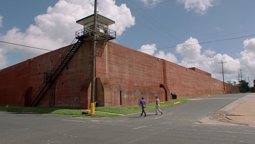 Richard Linklater walks with an unknown subject to a prison in Huntsville. The Texas filmmaker examines the prison industry in God Saves Texas.