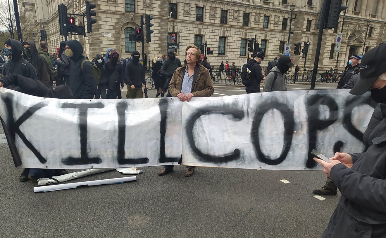 Barrett Brown holds the "Kill Cops" sign at a London protest against a new crime bill.