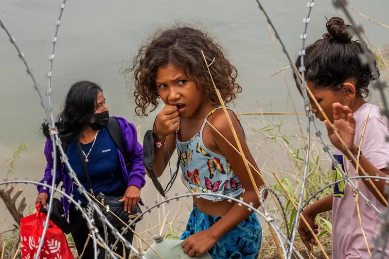 Image: Adults and children walk along razor wire covering the banks of the Rio Grande near Eagle Pass after illegally crossing over into the United States on June 14.